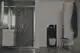Badezimmeransicht mit Dusche, Waschbecken, WC und Stuhl. Die Wände sind mit dunklem Fliesenmuster gestaltet. Ideal Standard Produkte sind im Raum integriert.